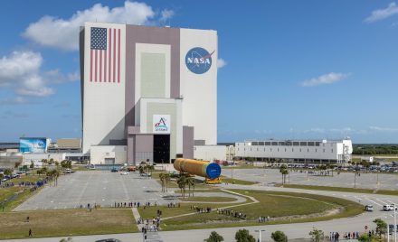 Велика помаранчева основна ступінь ракети SLS на платформі під час вивантаження з баржі Pegasus у Космічному центрі імені Кеннеді.